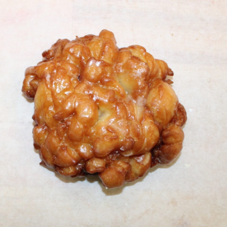 Golden brown glazed apple fritter on a light background.
