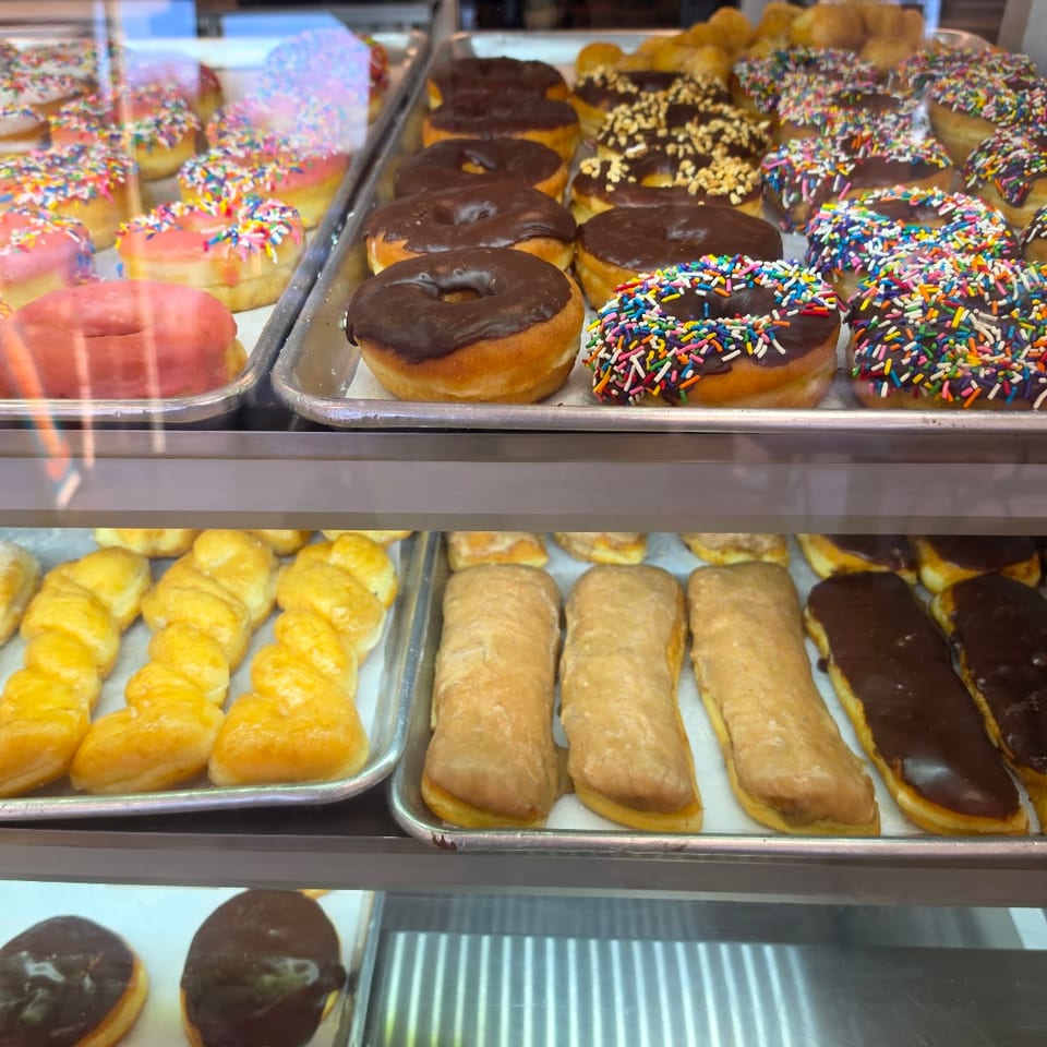 Multiple trays of colorful donuts and pastries displayed in a glass bakery case.