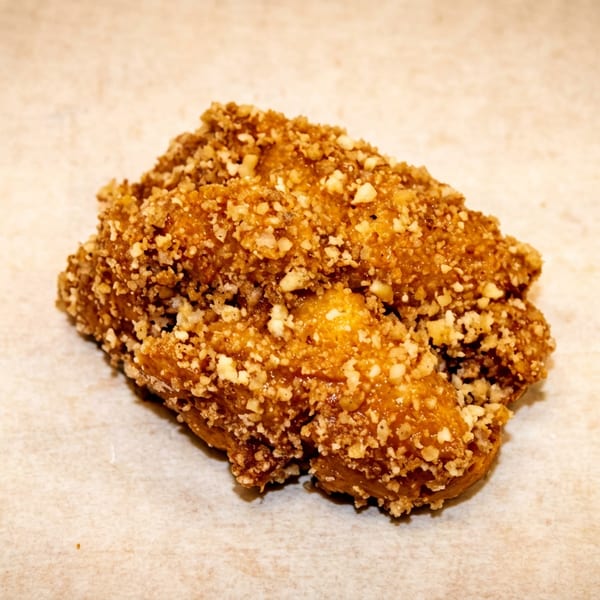 Golden brown dessert pastry with a crunchy nut topping on a light background.