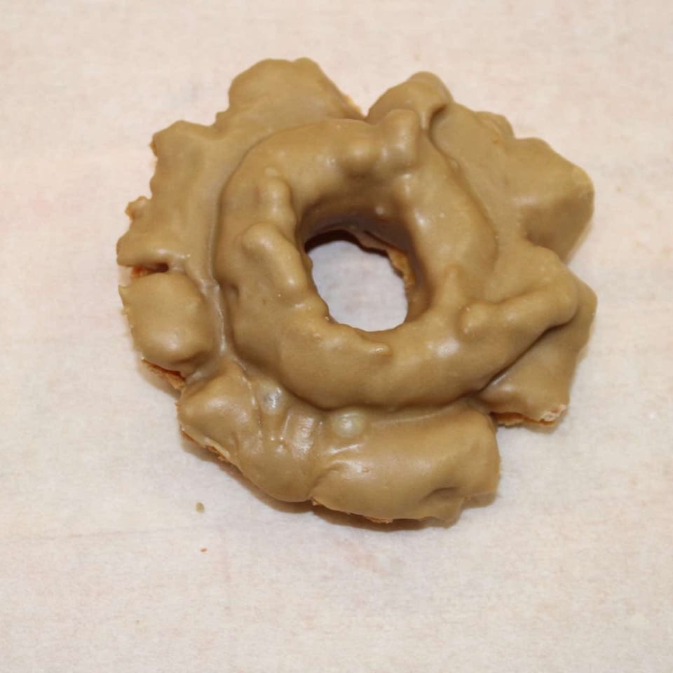 A single maple-glazed old-fashioned donut with a hole in the center, on a light background.